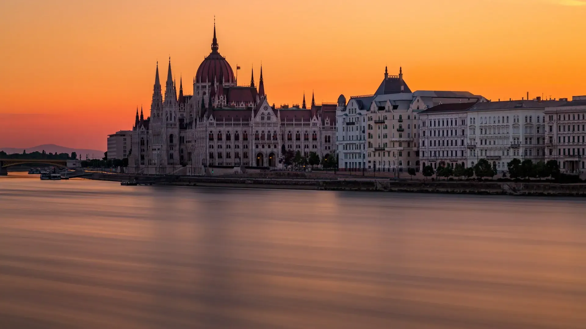 Parlamento de Budapest visto desde el Danubio al atardecer, con el cielo teñido de naranja