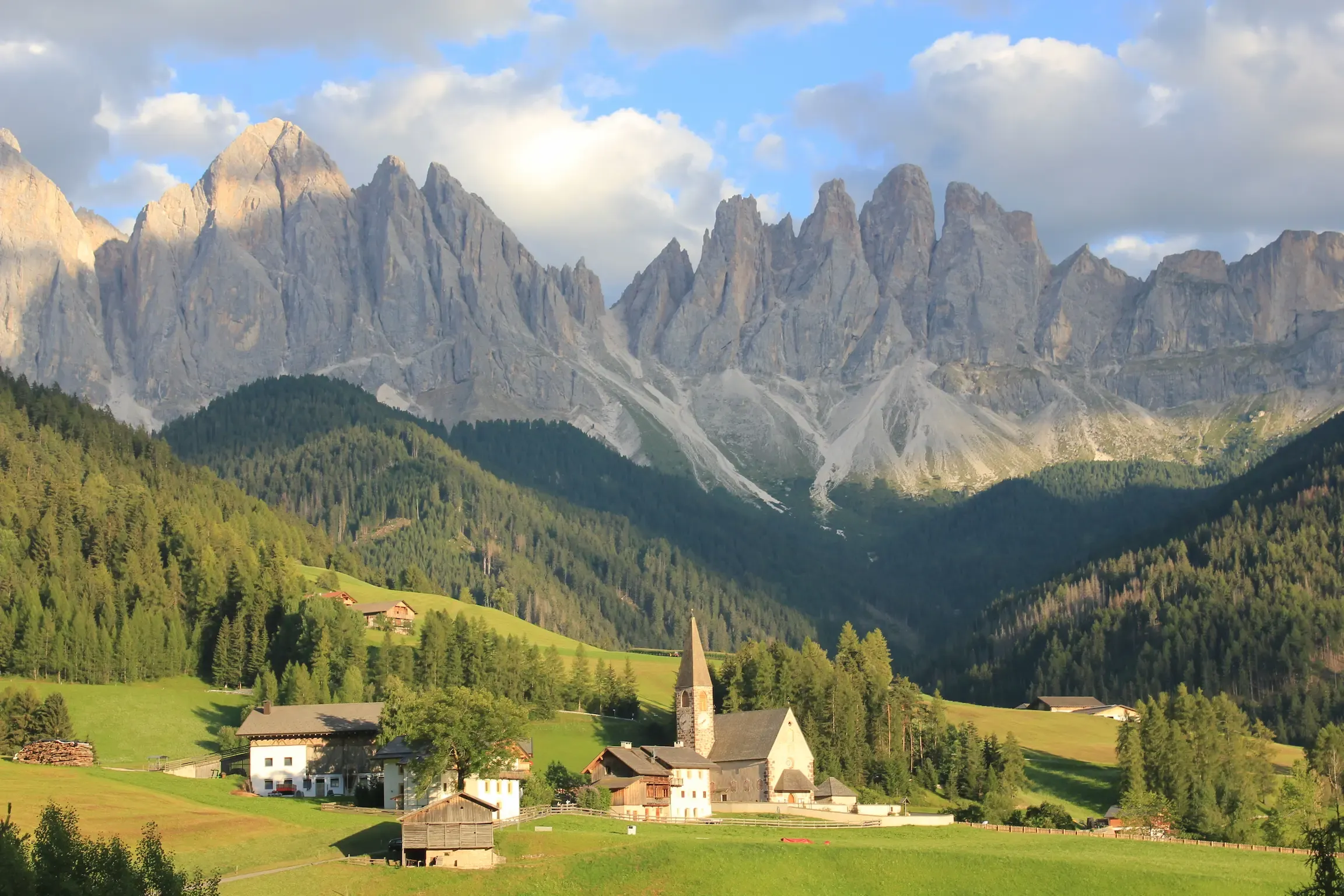 Pueblo alpino con iglesia de campanario ante las cumbres rocosas de las Dolomitas, Italia