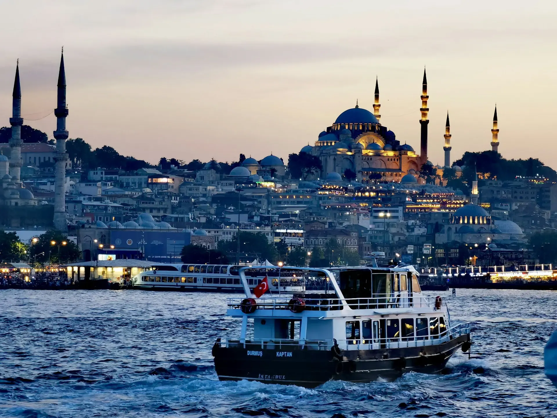 Barco navegando por el Bósforo al atardecer con la Mezquita de Solimán iluminada al fondo, Estambul