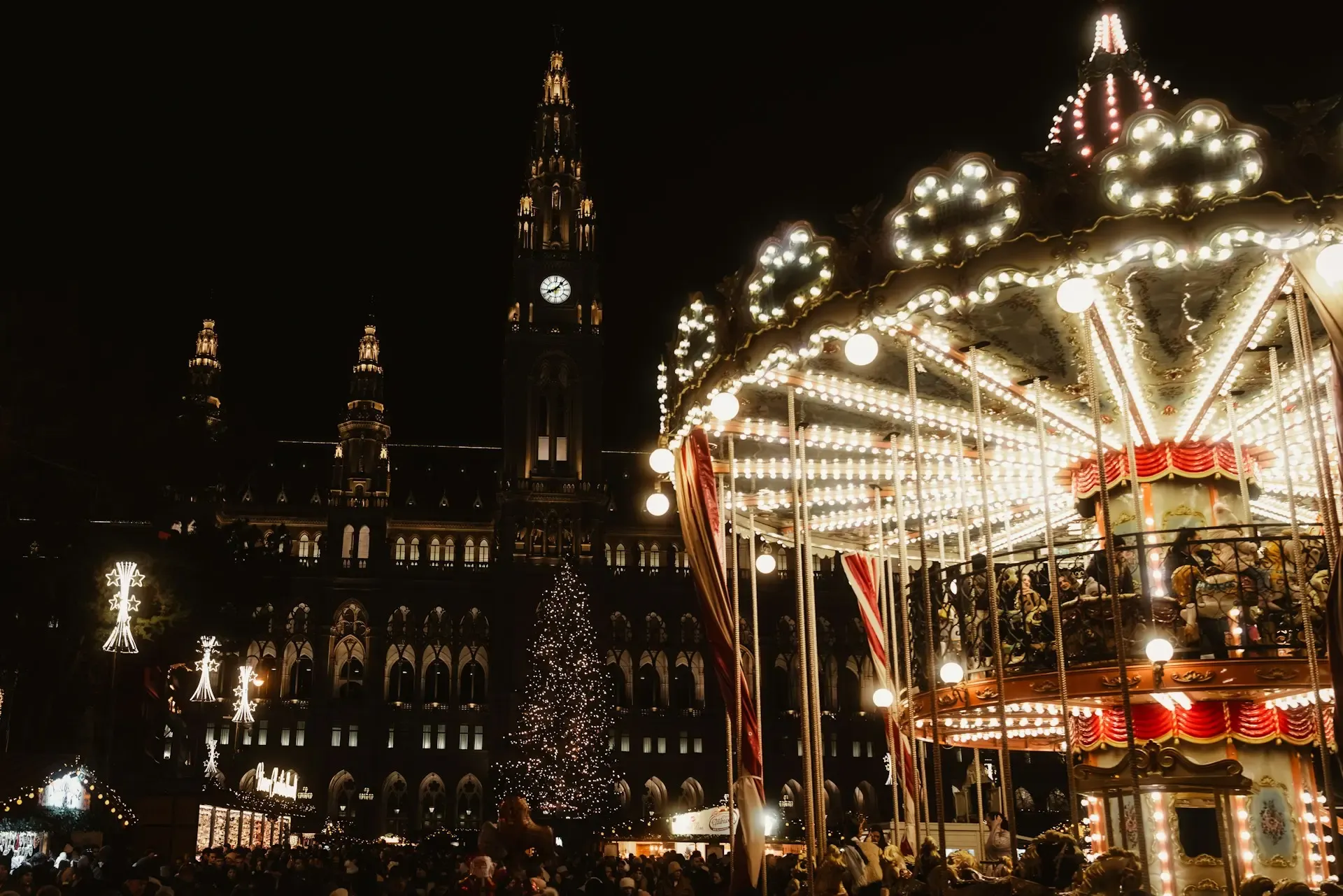 Mercadillo navideño frente al Ayuntamiento de Viena, con un carrusel iluminado y el árbol de Navidad de fondo