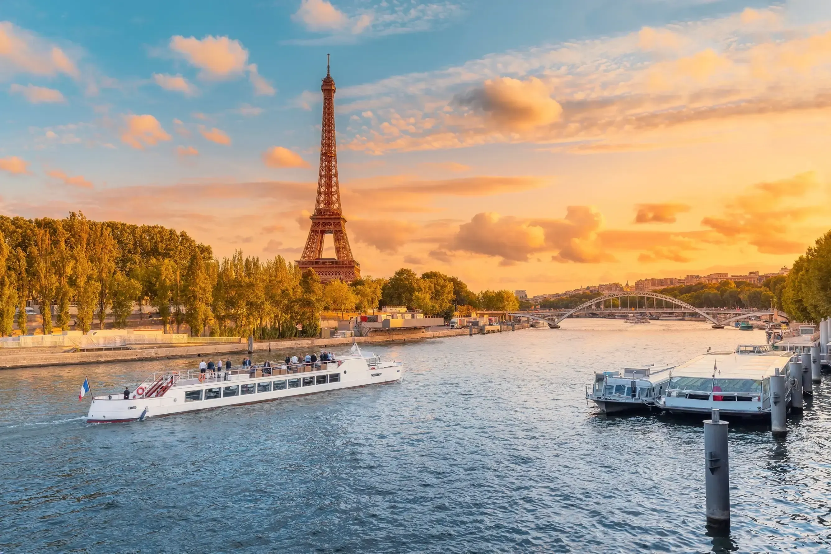 Torre Eiffel junto al Sena al atardecer, con barcos turísticos navegando por el río, París