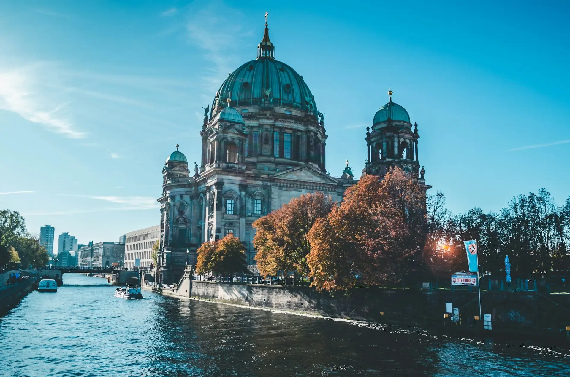 Catedral de Berlín con su cúpula verde junto al río Spree, rodeada de árboles en tonos otoñales