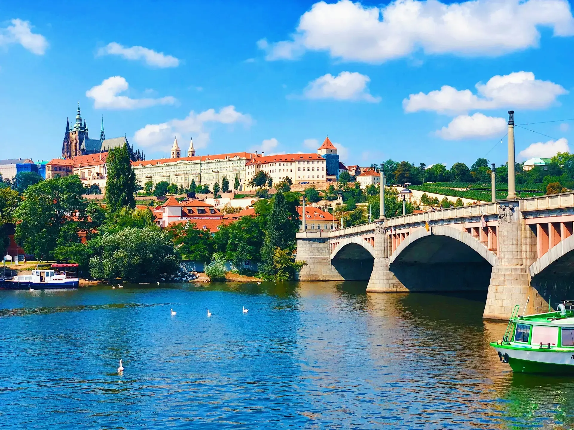 Castillo de Praga visto desde el río Moldava, con un puente y cisnes nadando en primer plano