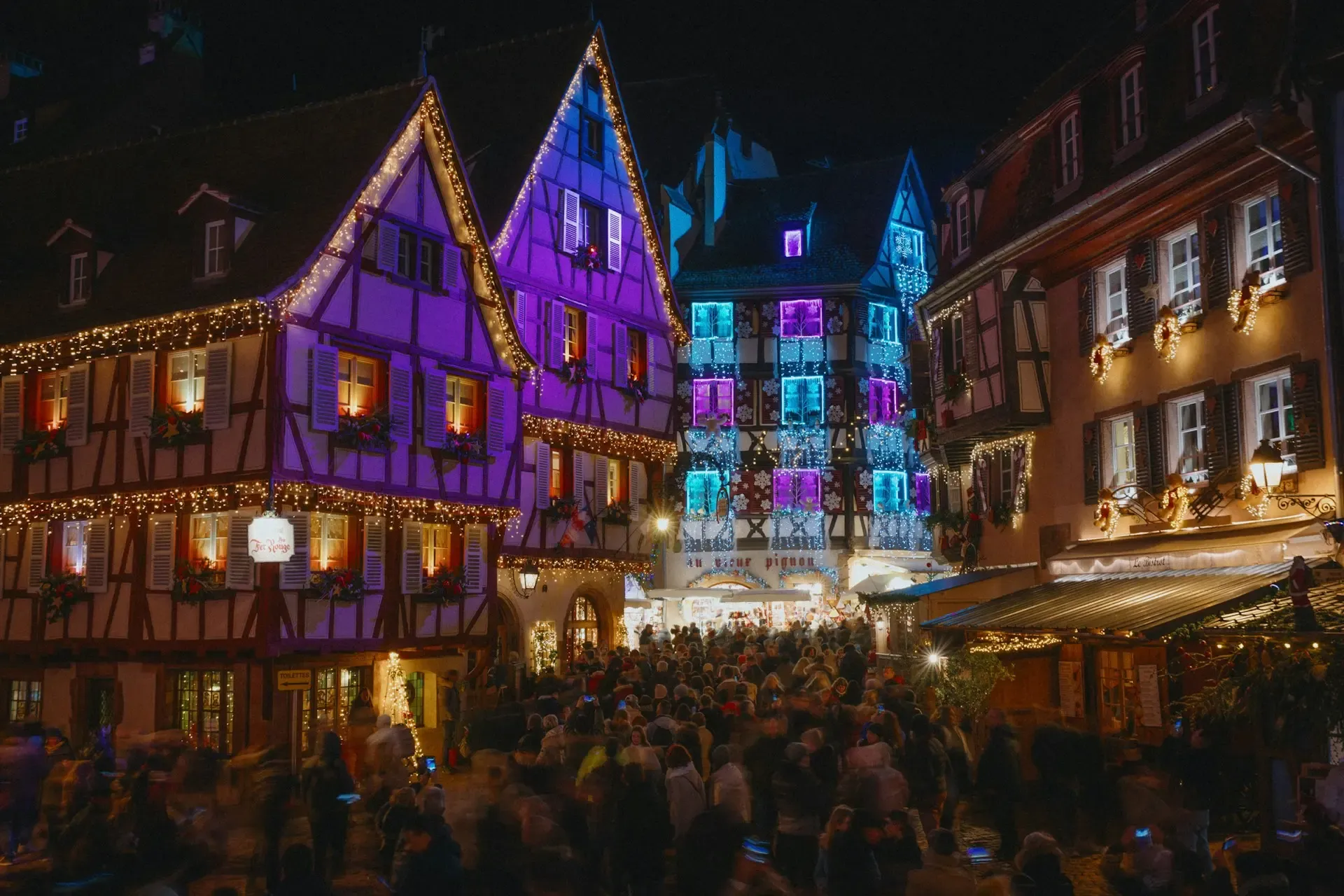 Casas de entramado de madera iluminadas de morado y azul en el mercado navideño de Colmar, Francia
