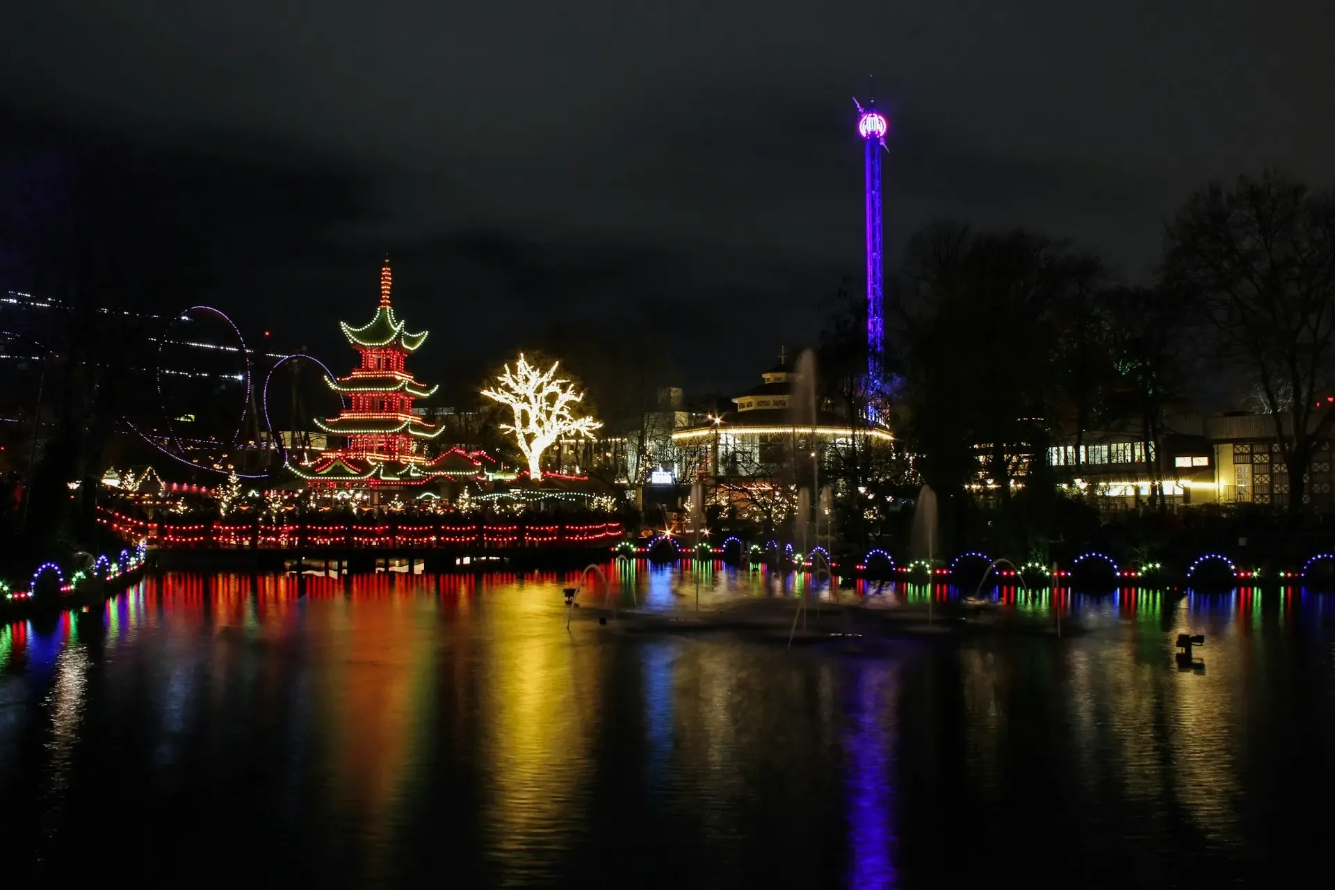 Jardines de Tivoli en Copenhague iluminados de noche, con la pagoda china y las fuentes reflejadas en el agua