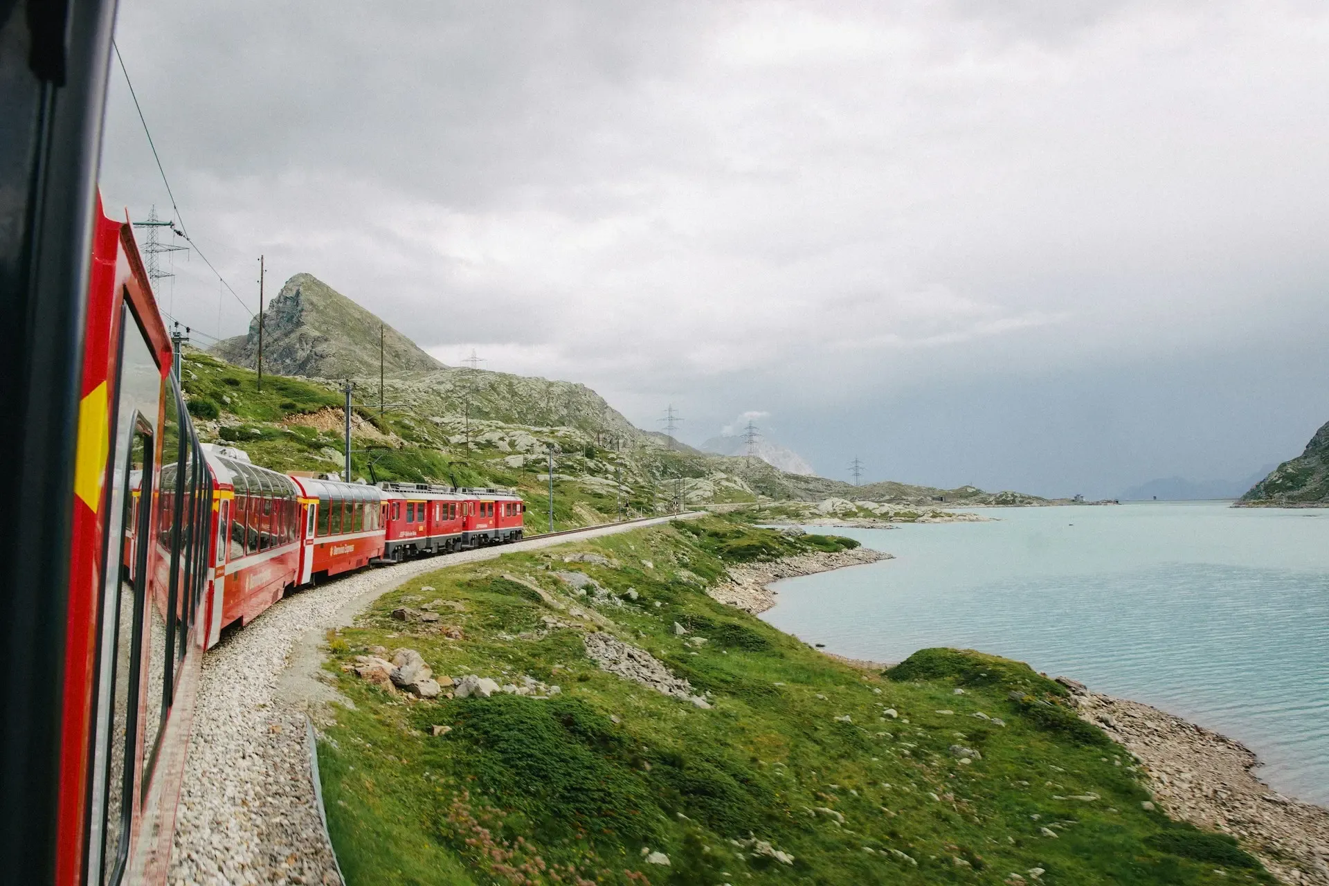 Tren rojo del Bernina Express circulando junto a un lago alpino turquesa, con montañas al fondo