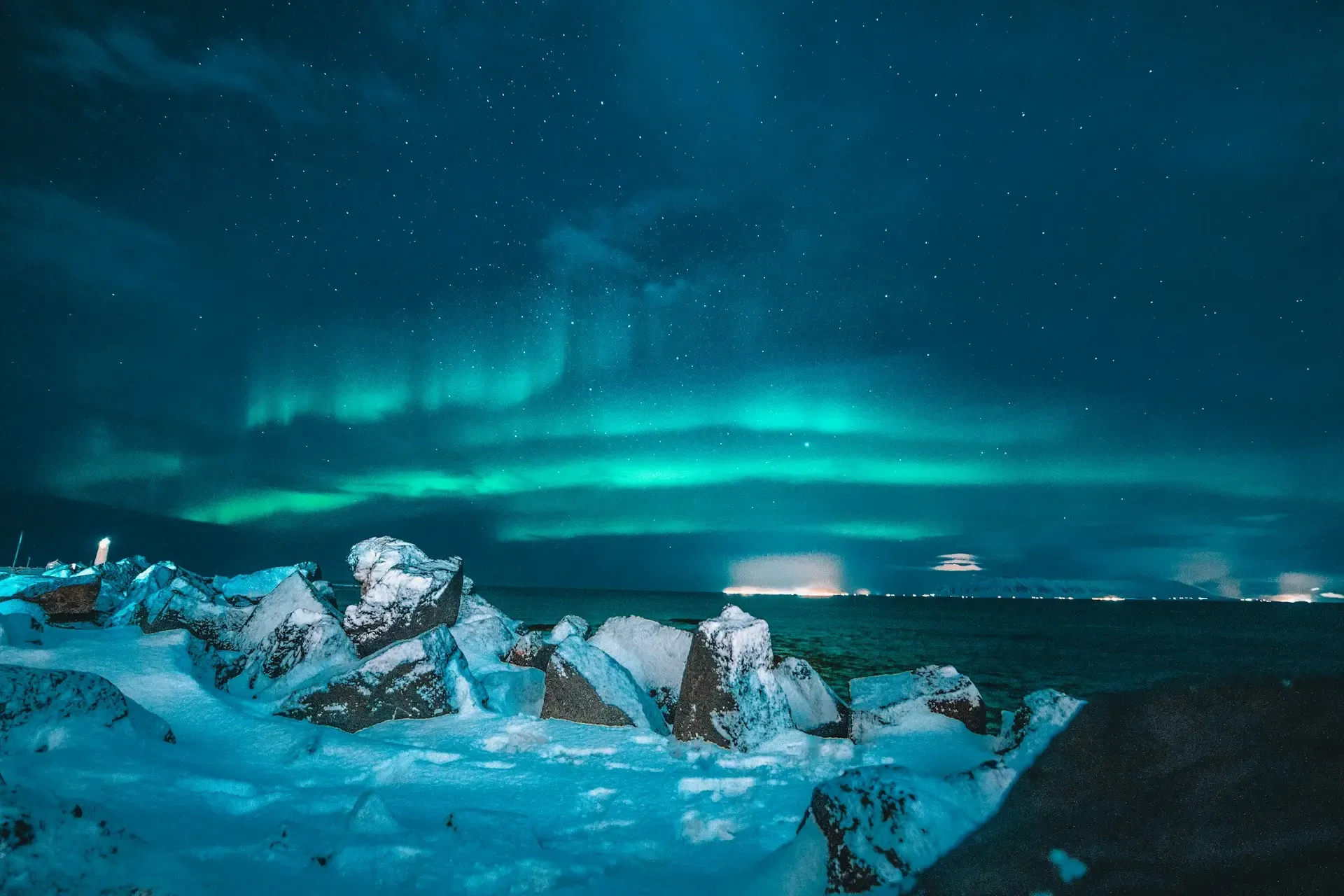 Auroras boreales verdes sobre el mar y rocas nevadas en una noche estrellada en Islandia