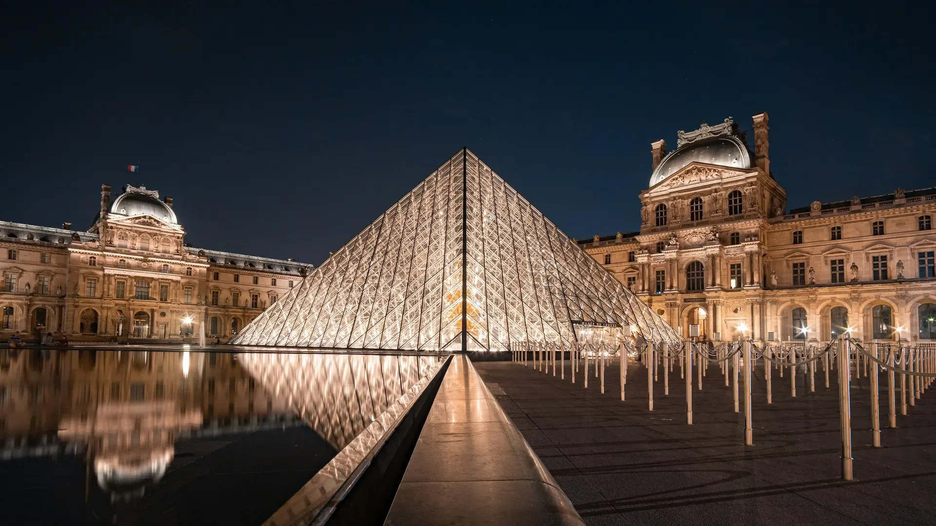 Pirámide de cristal del Museo del Louvre iluminada de noche junto al estanque, París