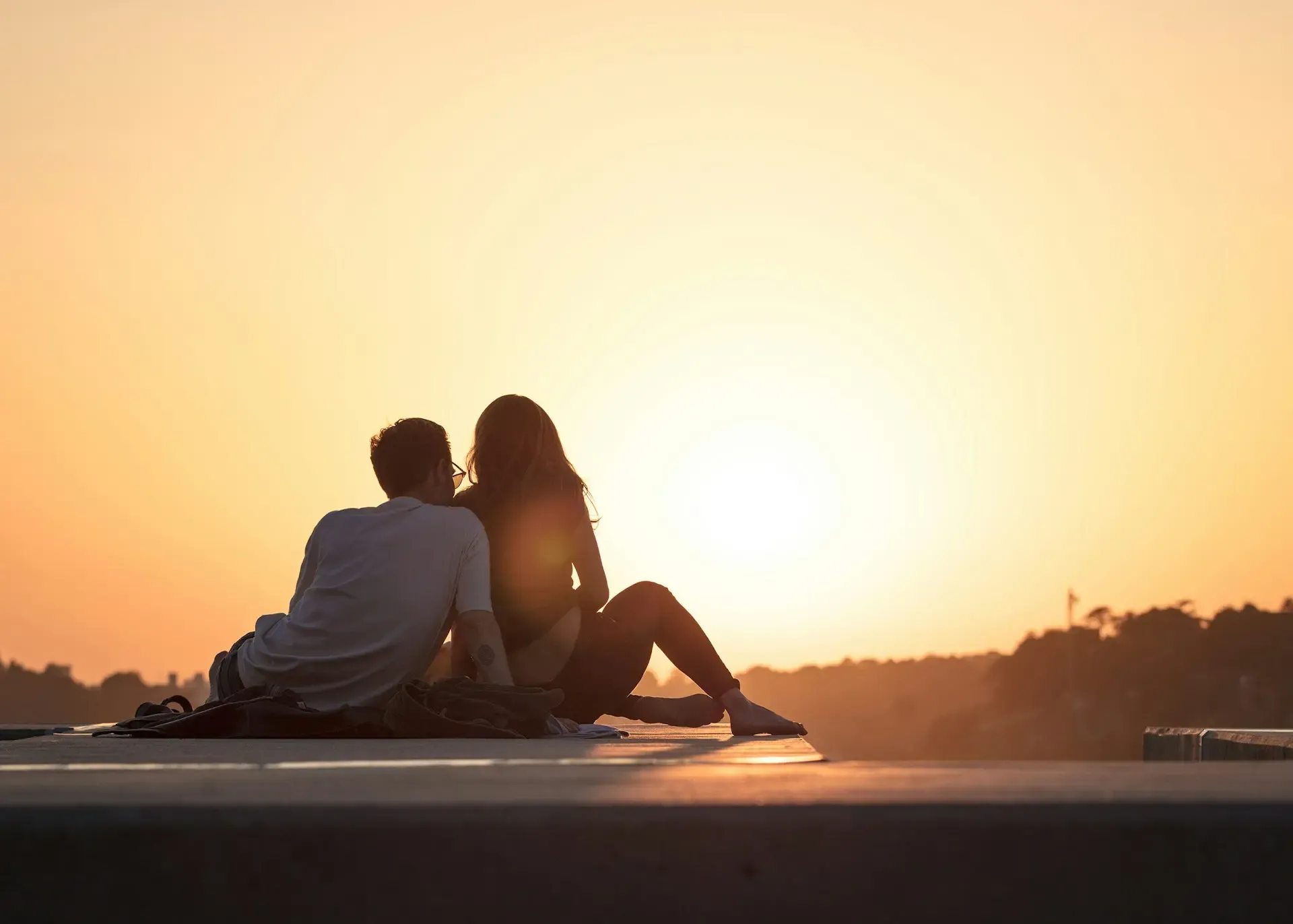 Pareja en silueta contemplando juntos la puesta de sol dorada