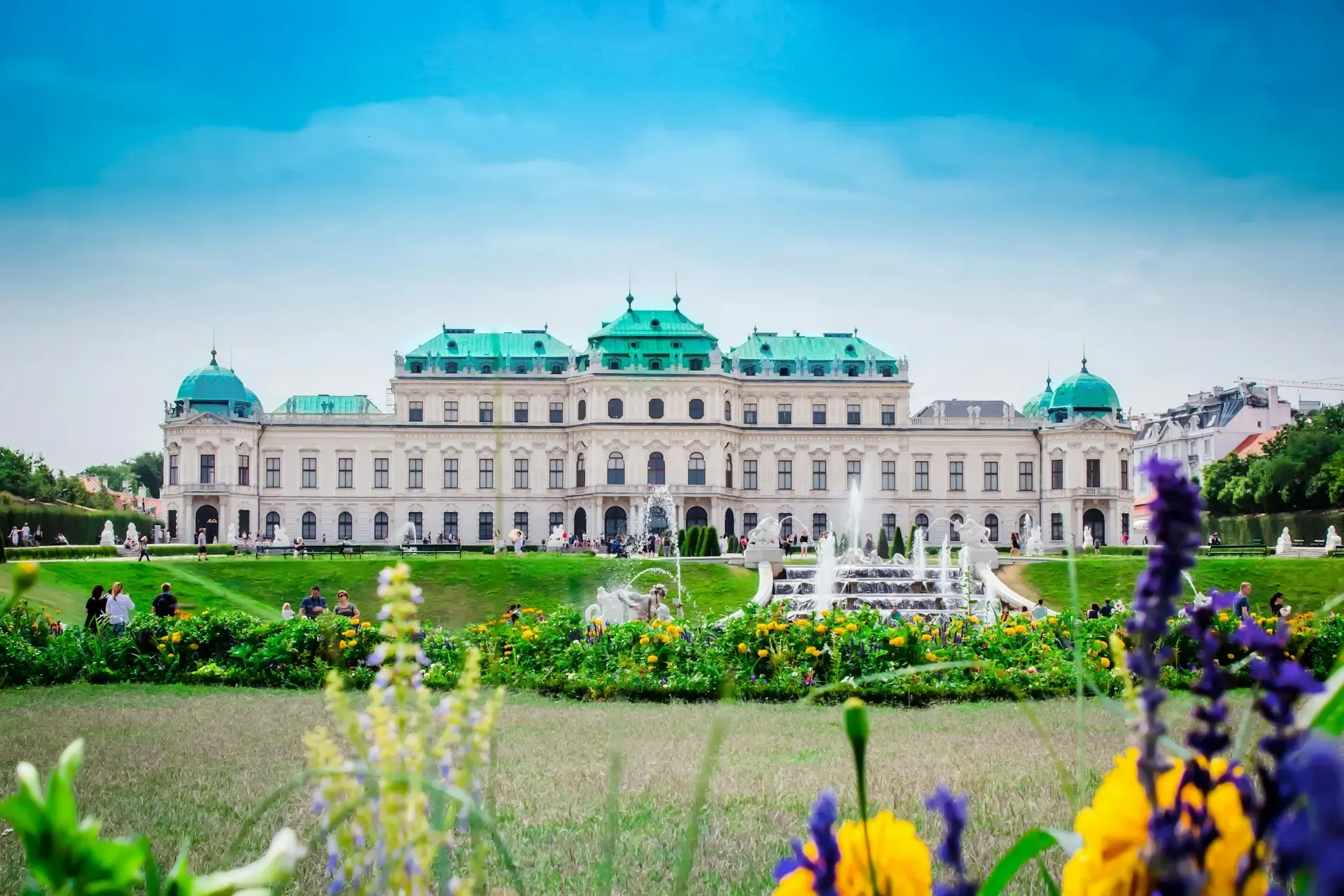 Palacio del Belvedere en Viena con sus tejados verdes, rodeado de jardines floridos y una fuente en primer plano